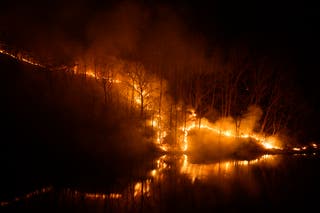 Smoke rises from burning trees as a wildfire is reflected in the waters of the Nakdong River in Andong